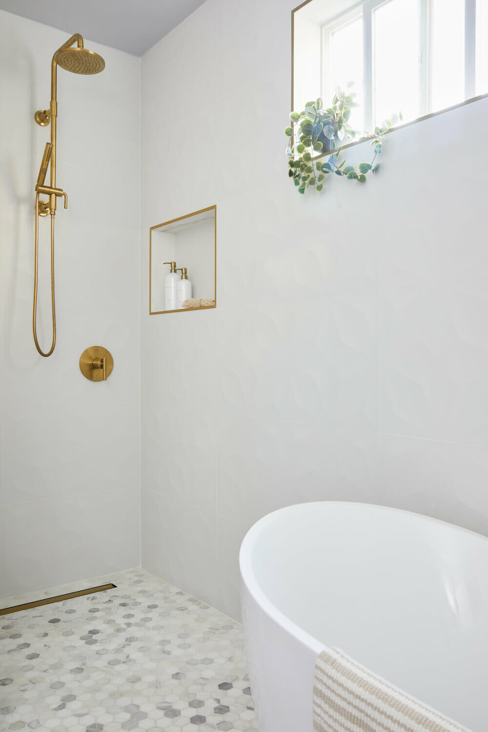 stand-in shower with brushed gold shower head and fixtures and recessed shelf with gold frame and white walls and free standing bathtub after renovation